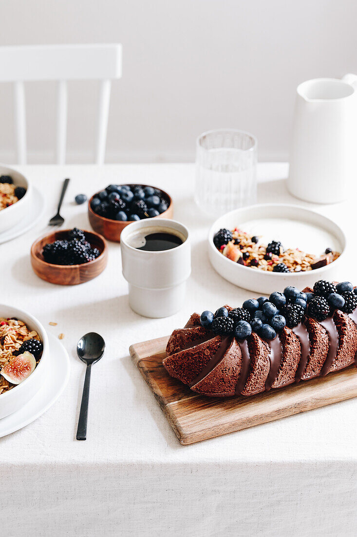 Frühstückstisch mit Joghurt-Bowls, Beeren und Schokoladenkuchen
