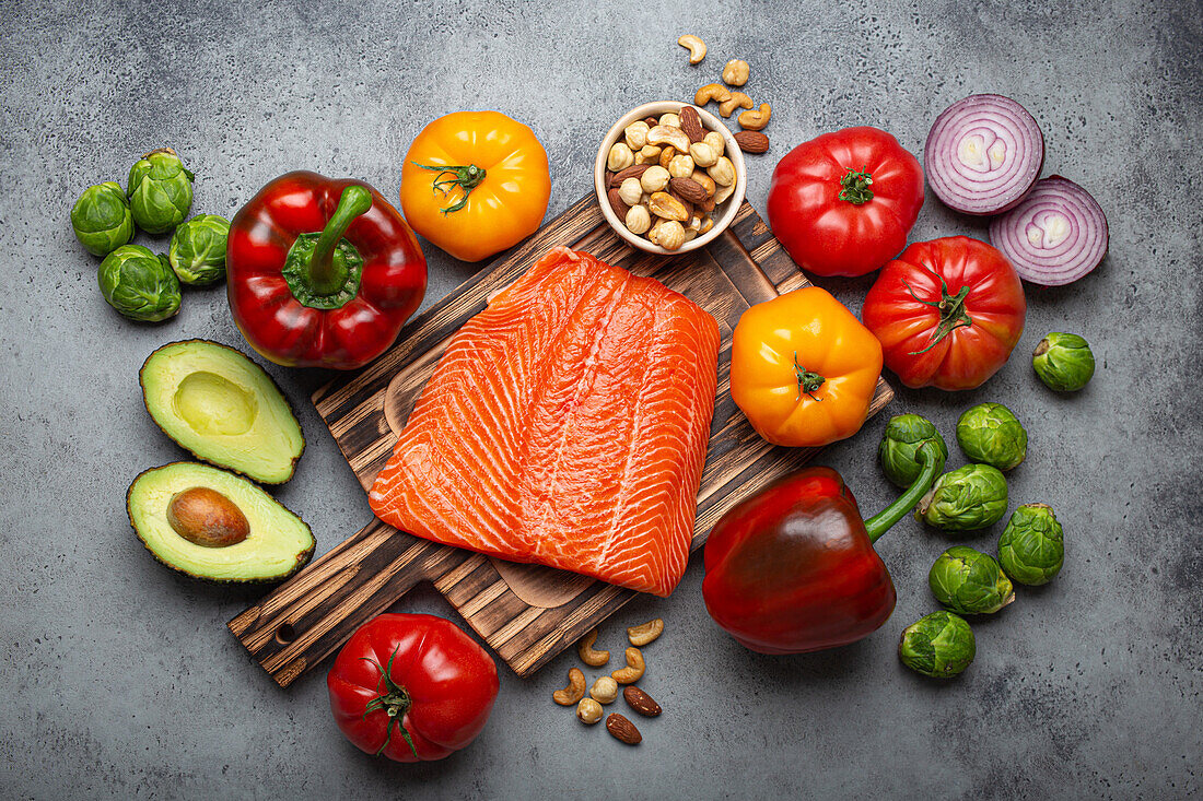 Fresh salmon fillets on a wooden cutting board, with organic vegetables and nuts