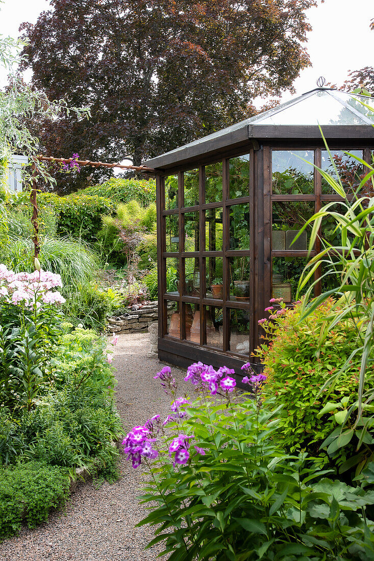 Glashaus umgeben von blühendem Garten im Sommer