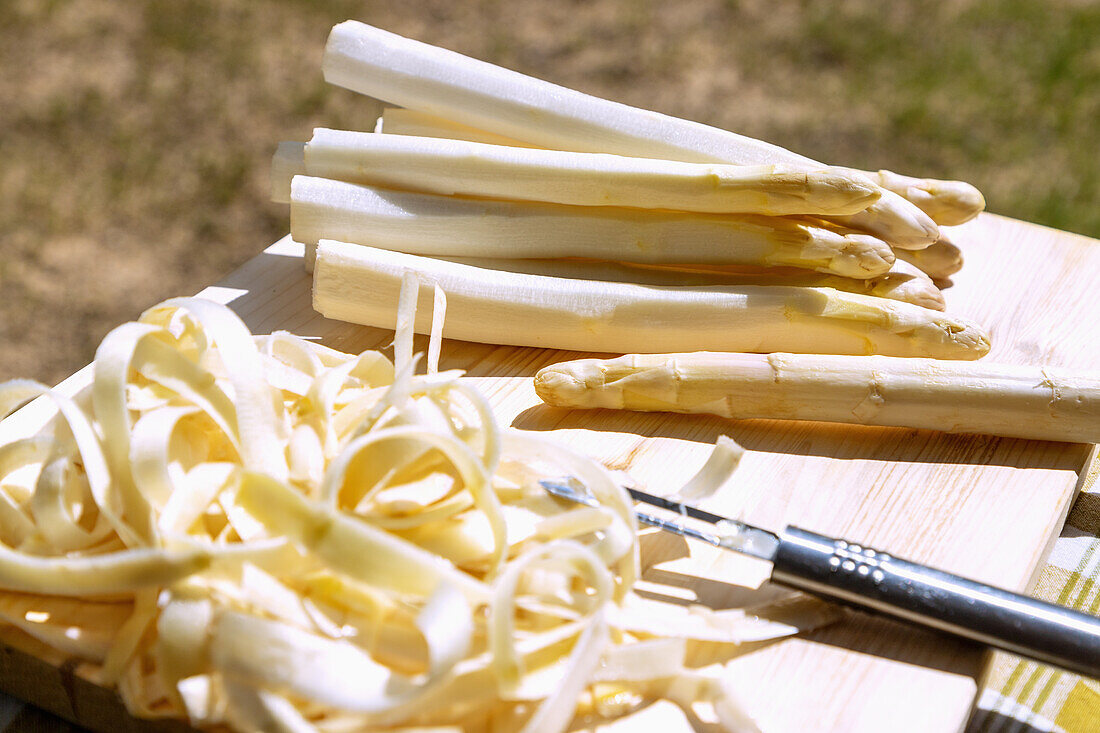 White asparagus, peeled, with a peeler on a wooden board outside