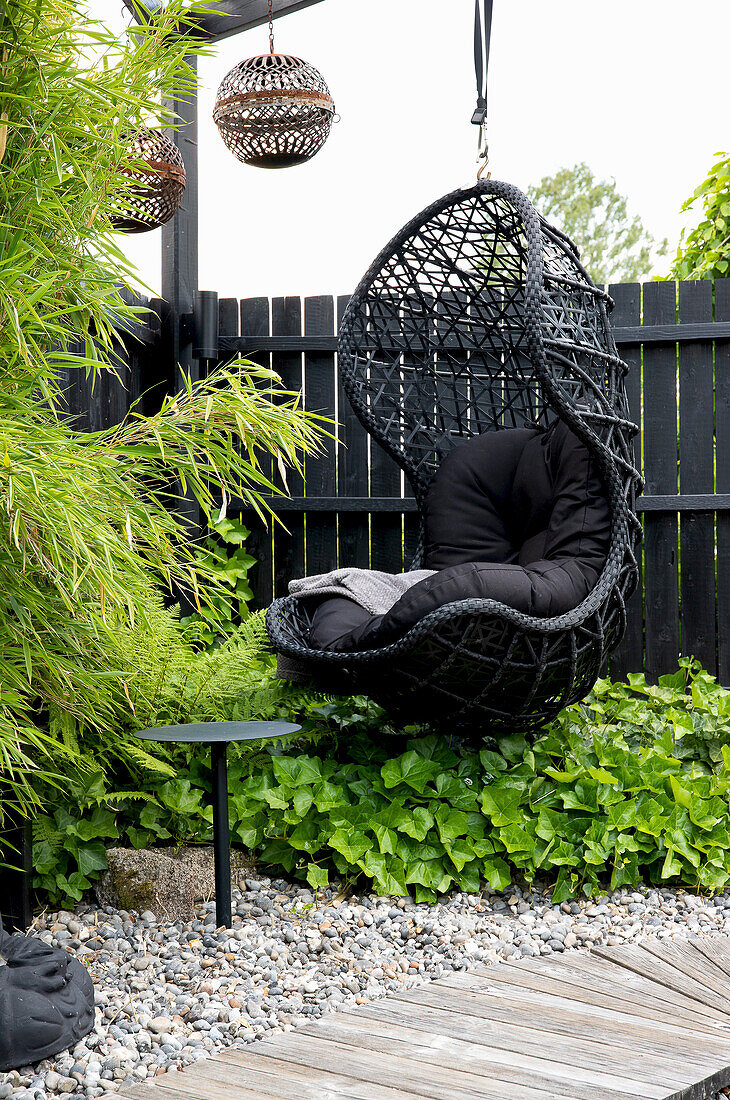 Schwarzer Hängesessel aus Rattan mit Kissen im modern gestalteten Gartenbereich
