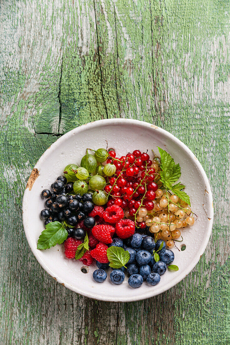 Fresh berries with leaves in vintage ceramic strainer on green rustic wooden background