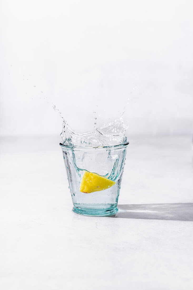 Zitrone fällt spritzend in ein Glas Wasser