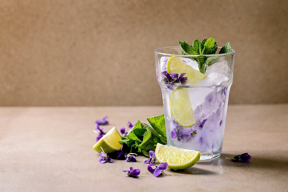 Lemonade soda cocktail with mint, ice cubes with violet blossoms and lime slices