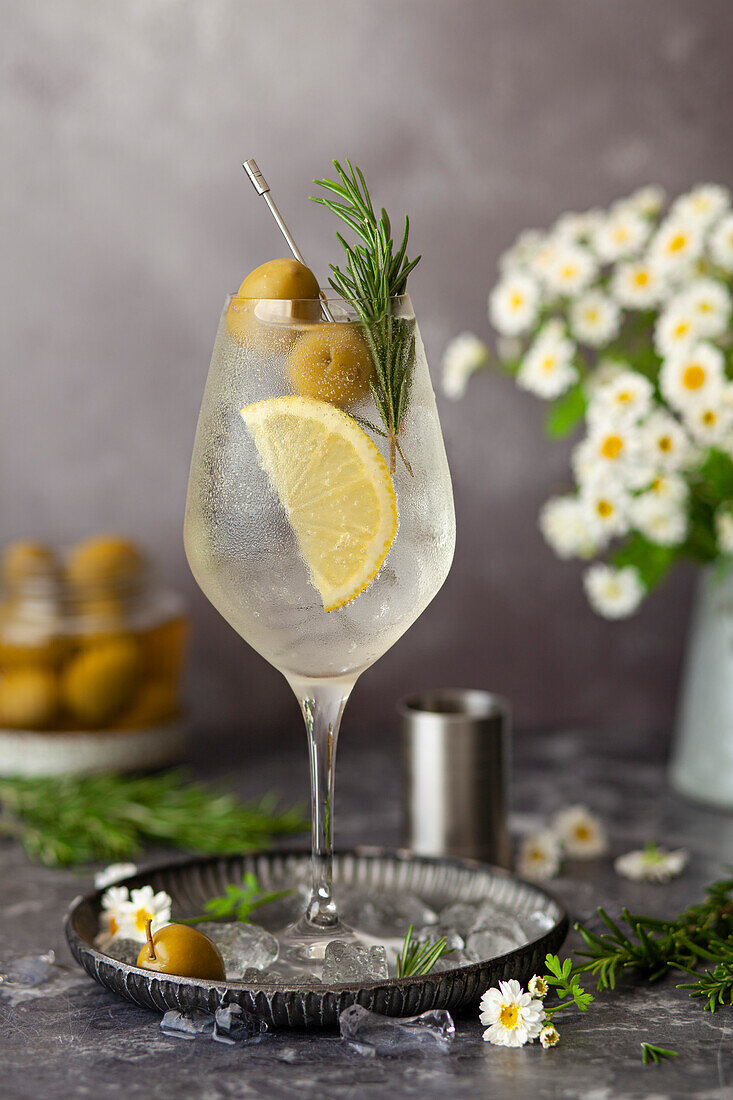 Italian white spritz cocktail made with Bianco bitter liqueur garnished with lemon, olives and rosemary