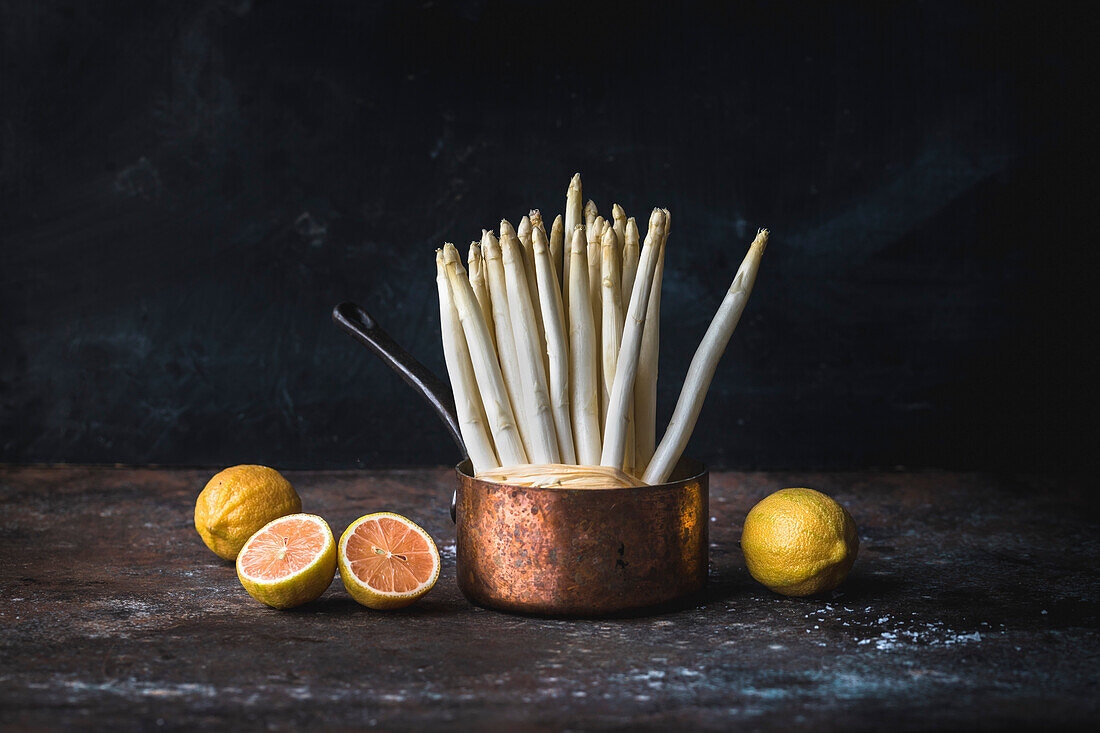 White asparagus spears in a copper pot next to pink lemons