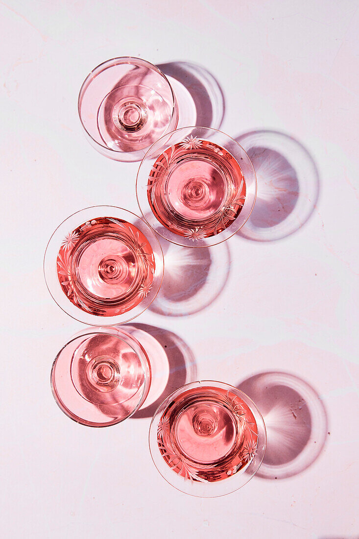 Gläser mit Roséwein auf rosafarbenem Untergrund mit Lichtreflexion