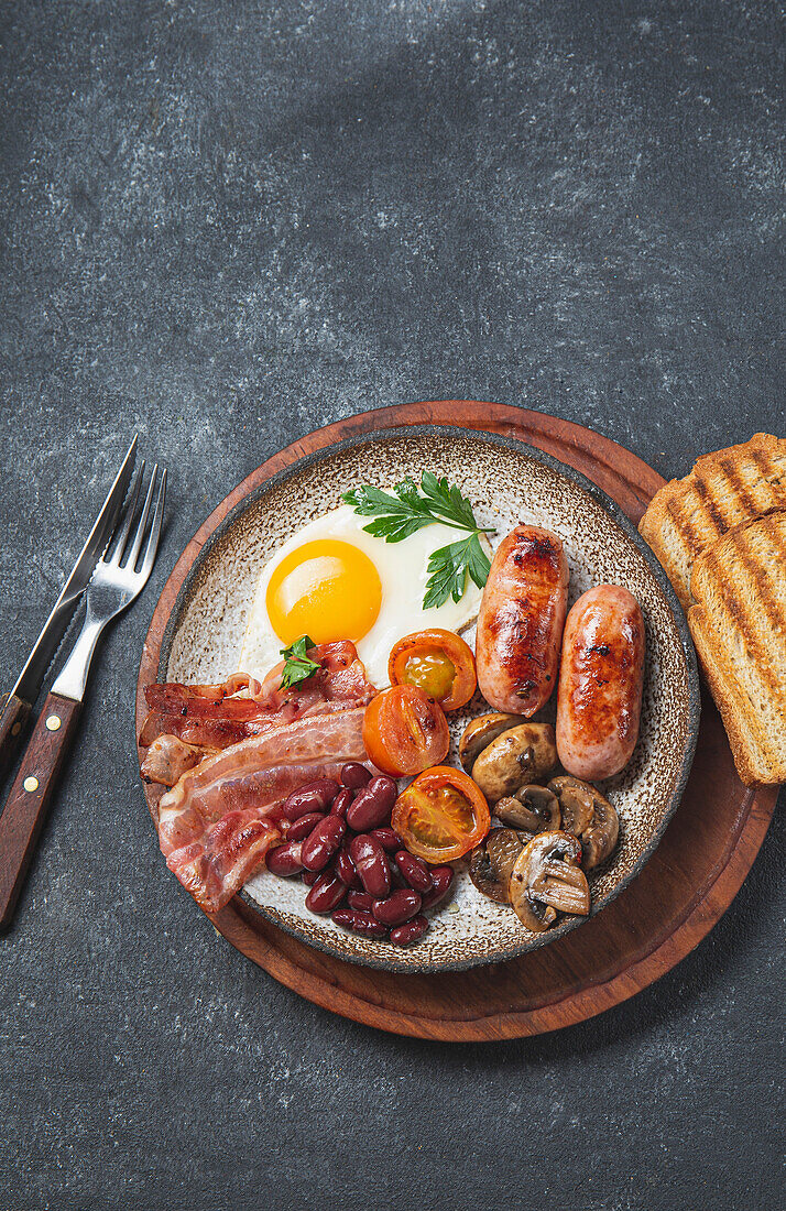 Englisches Frühstück mit Spiegeleiern, Würstchen, Bohnen, Pilzen, gegrillten Tomaten, Speck und Toast