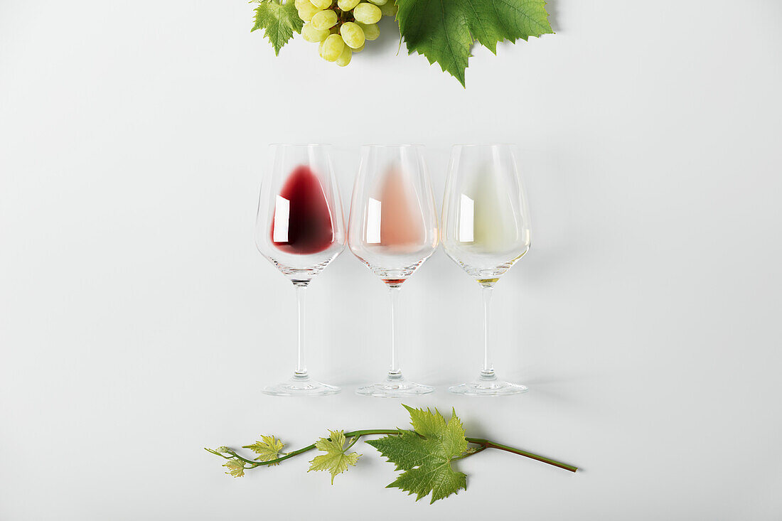 Rot-, Rosé- und Weißwein in Gläsern, Weinblätter und Weinflaschen auf weißem Hintergrund