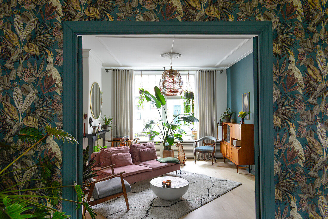 Living room with large houseplant, pink sofa and patterned wallpaper