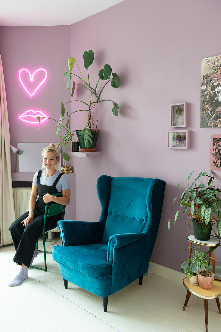 Wall in purple, neon signs in heart and lip shape, wing chair in blue and houseplants