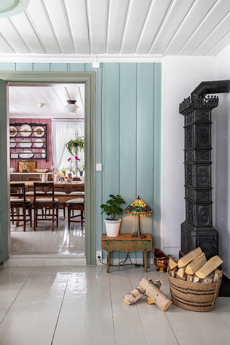 Fireplace, basket with firewood, open door with view of dining table and chairs, wall shelf with plates