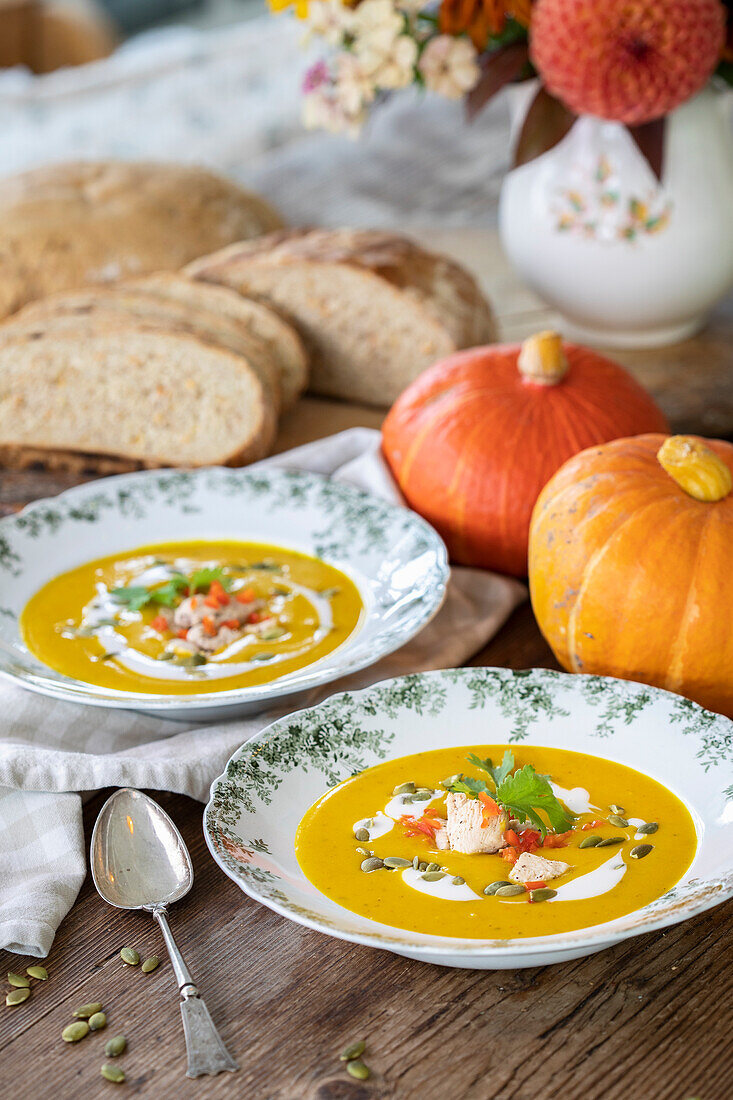 Kürbissuppe in Suppentellern mit Kürbiskernen und Petersilie garniert, Brot und Kürbisse