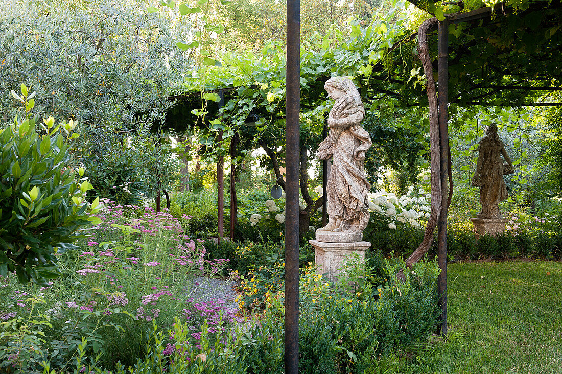 Statuten im Garten und mit Wein bewachsene Pergola