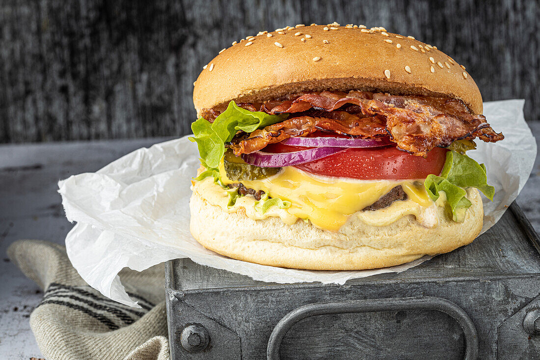 Cheeseburger mit Rind, Speck, Tomaten, roten Zwiebeln und Gewürzgurken