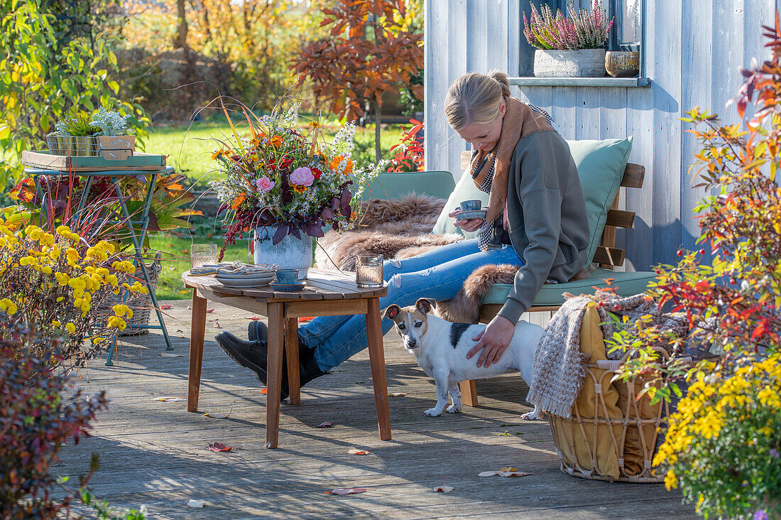 Woman on autumnal terrace with dog and flower decoration