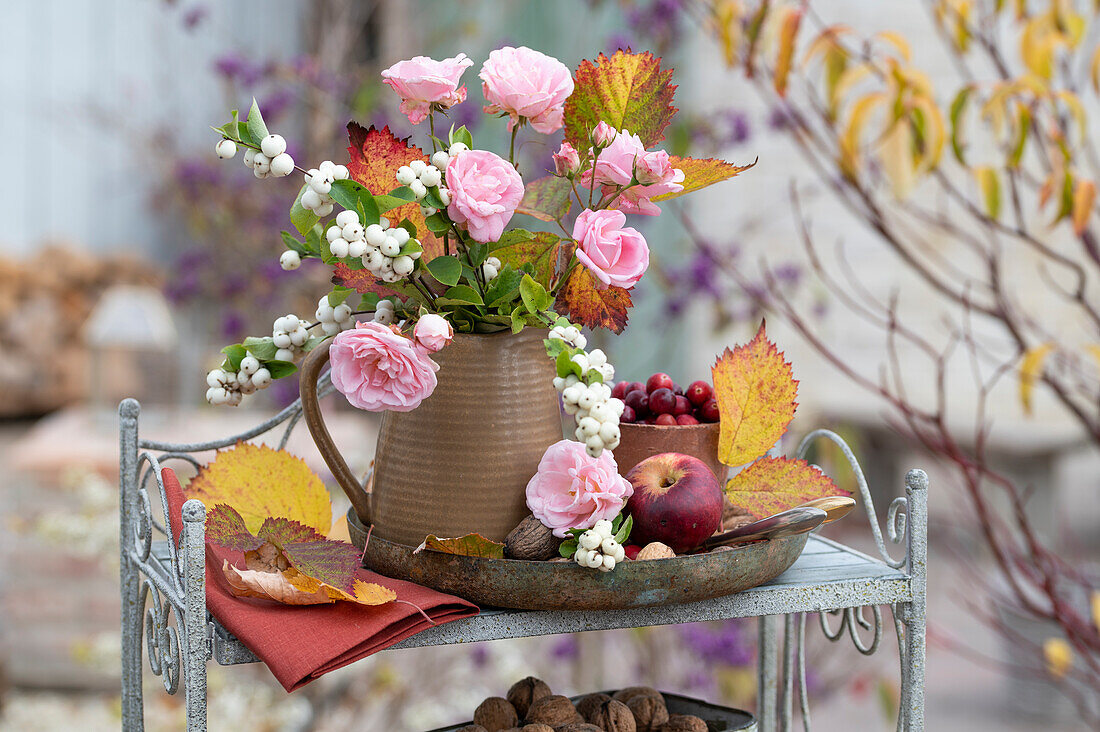 Herbstlicher Blumenstrauß aus Schneebeere (Symphoricarpos), Rosen und Herbstlaub auf Regal