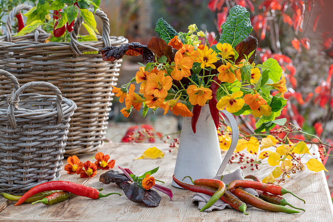 Autumn bouquet of marigolds (Calendula), nasturtiums (Tropaeolum), chard leaves and chilli peppers on patio table