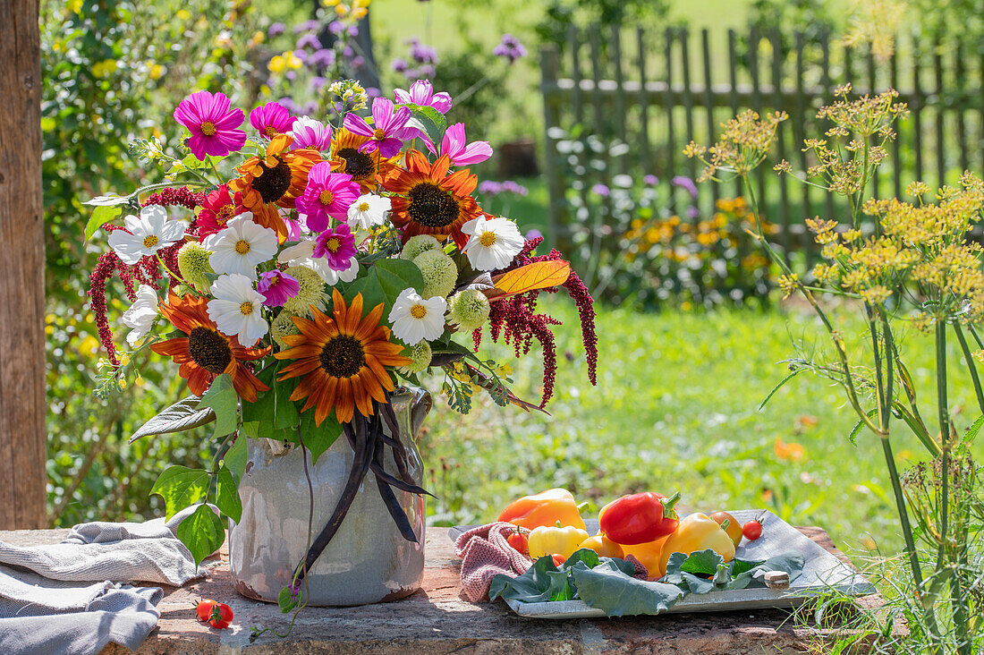 Blumenstrauß aus Sonnenblumen 'Samtkönigin' (Helianthus), Sonnenhut 'Delicous Nougat' (Echinacea), Cosmea (Cosmos), Rosen 'Double Delight' (Rosa), Zinnien (Zinnia), Stangenbohne 'Blaue Hilde', Brokkoli, Paprika  auf Gartentisch