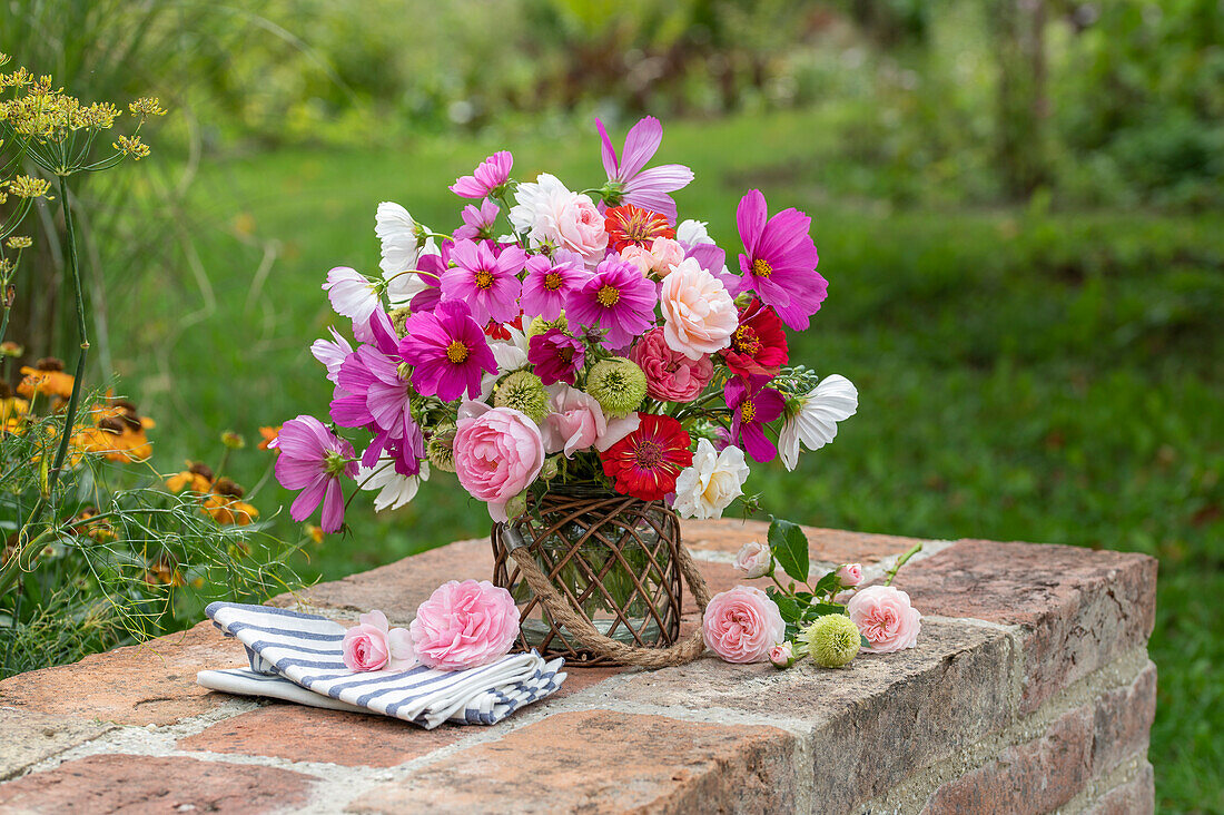 Bouquet of cosmea (Cosmos), zinnias (Zinnia), roses 'Double Delight' (Rosa) on garden wall, coneflower (Echinacea) in flower bed