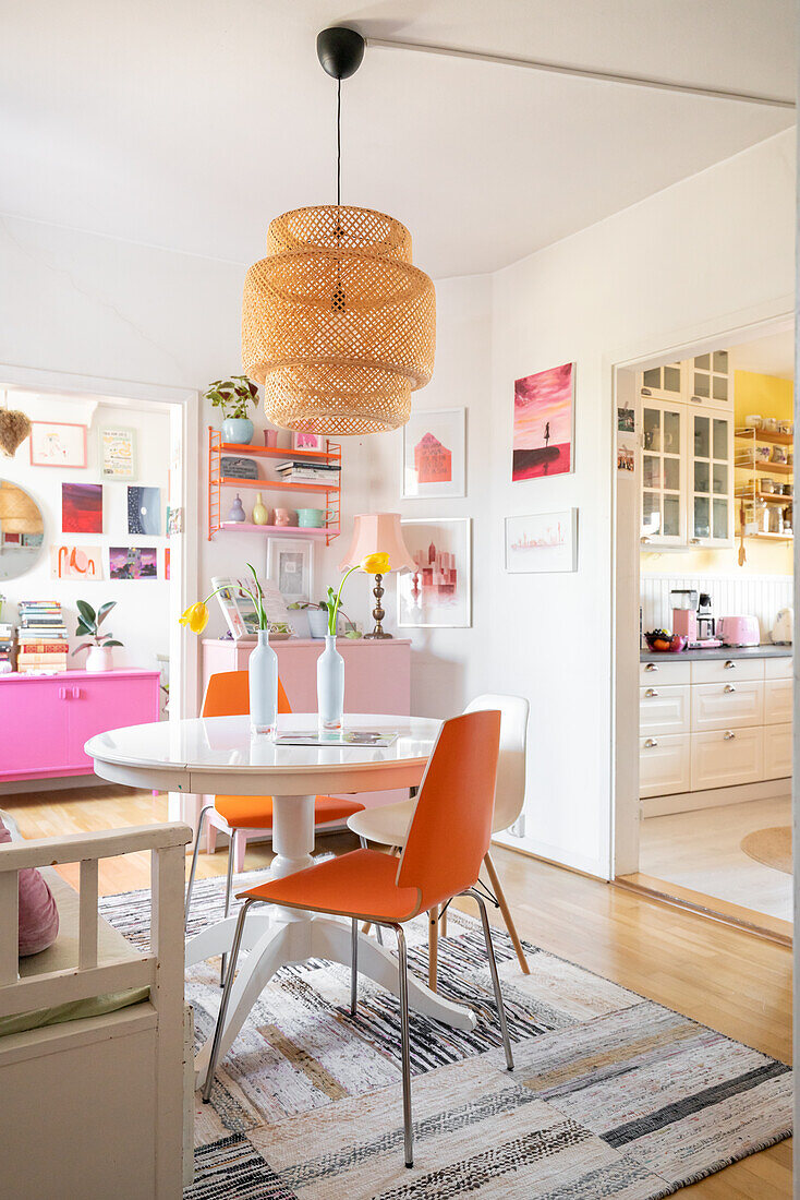 Dining area with white table, orange-coloured chairs and bamboo ceiling lamp