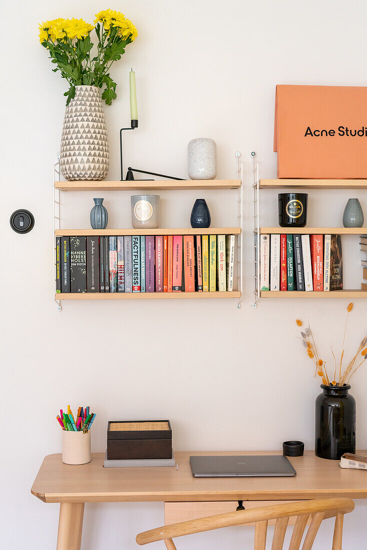 Wall shelf with books and decor above workstation with laptop and pens