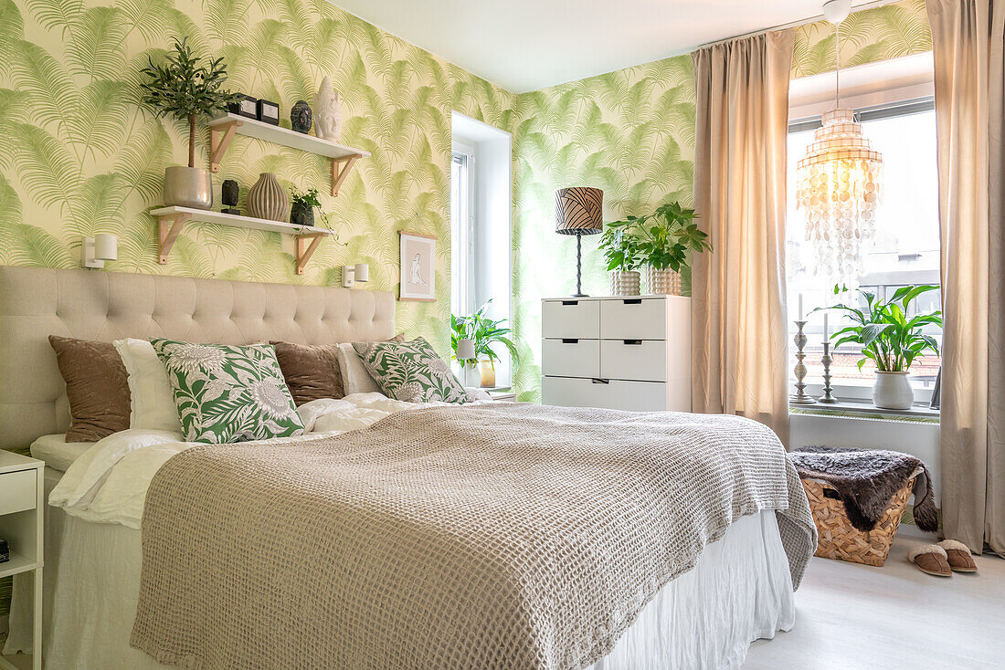 Light green bedroom with plant pattern wallpaper and bed in earthy tones