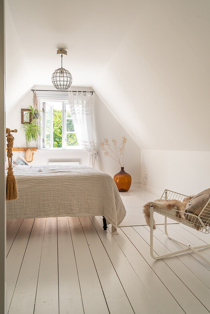 Bright attic bedroom with white floorboards and a view of trees out the window