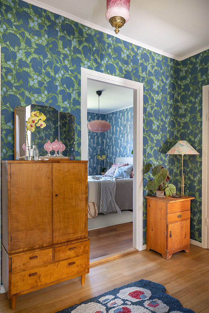 Vintage wooden chests of drawers, floral wallpaper and wooden floor, view into the bedroom