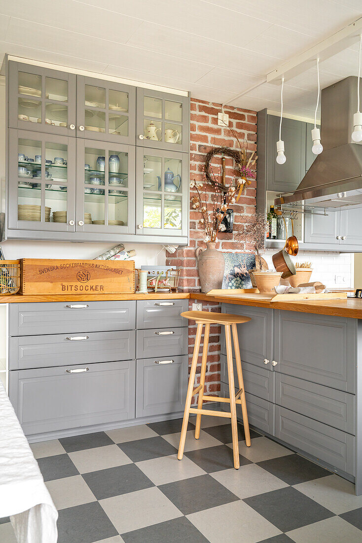 Kitchen with grey cabinets, chequerboard floor and brick wall