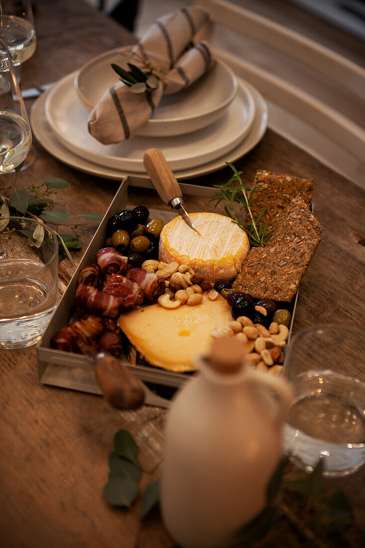 Platte mit Käse, Nüssen, Oliven und Datteln im Speckmantel auf rustikalem Holztisch