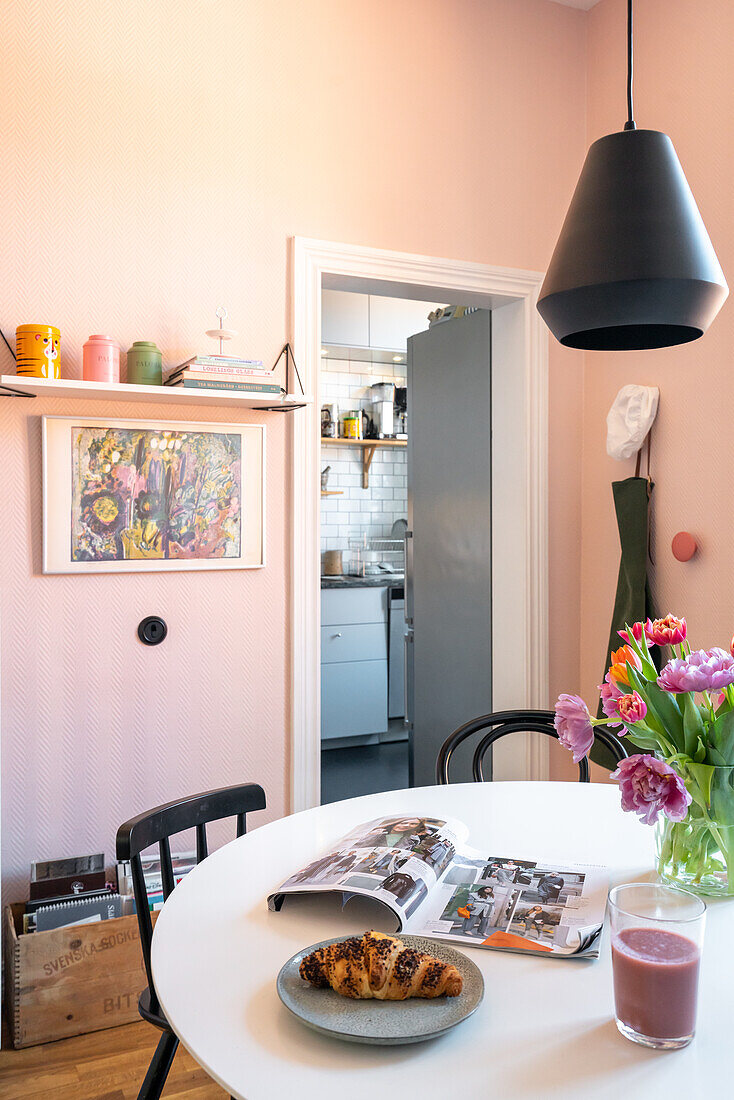 Dining table with bouquet of tulips and modern pendant light in dining room, view of kitchen