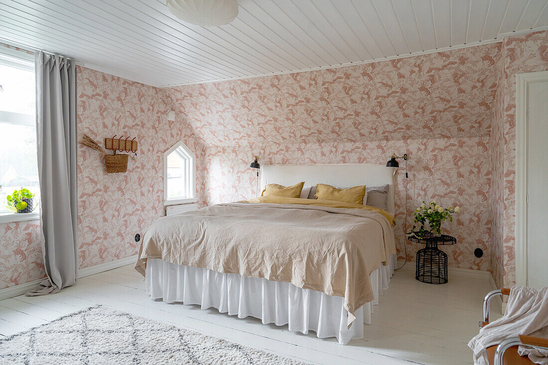 Bedroom with floral wallpaper, sloping ceiling and white bed skirt with ruffles