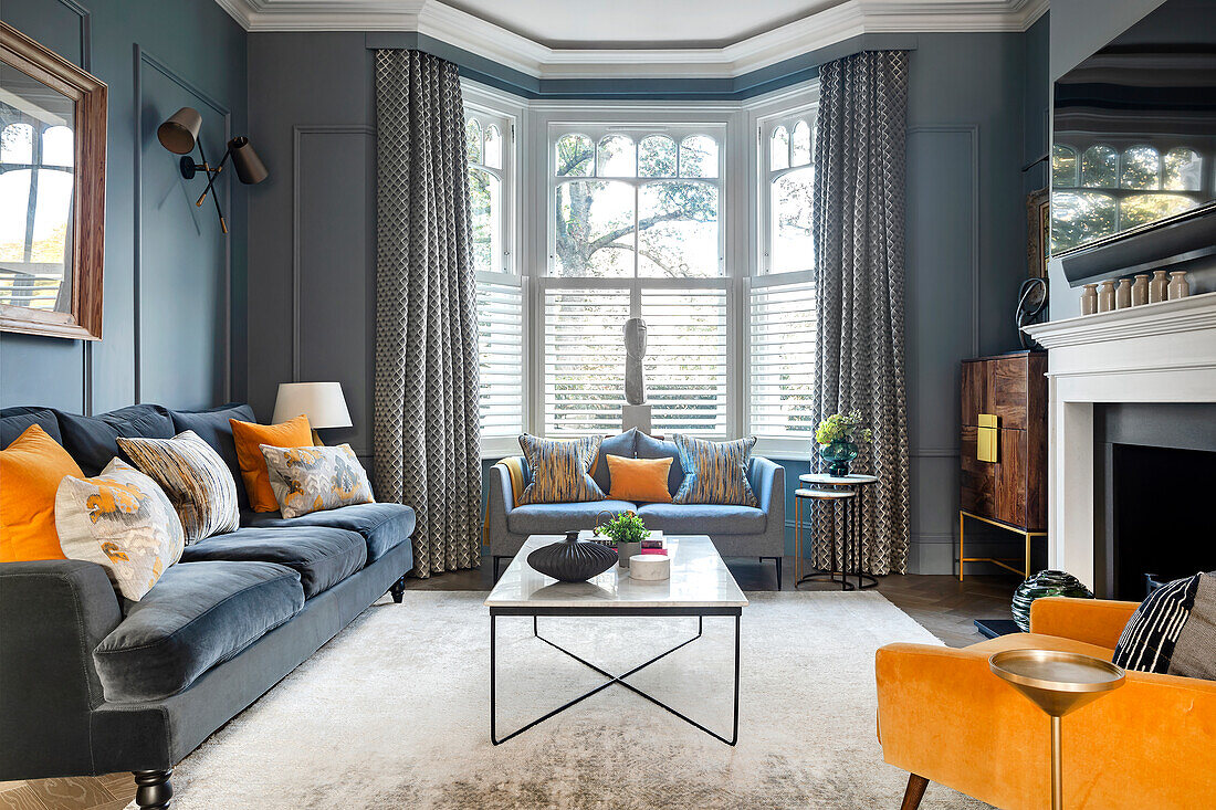 Classic living room with blue walls, color-matching velvet sofa, yellow accents, fireplace and bay window area