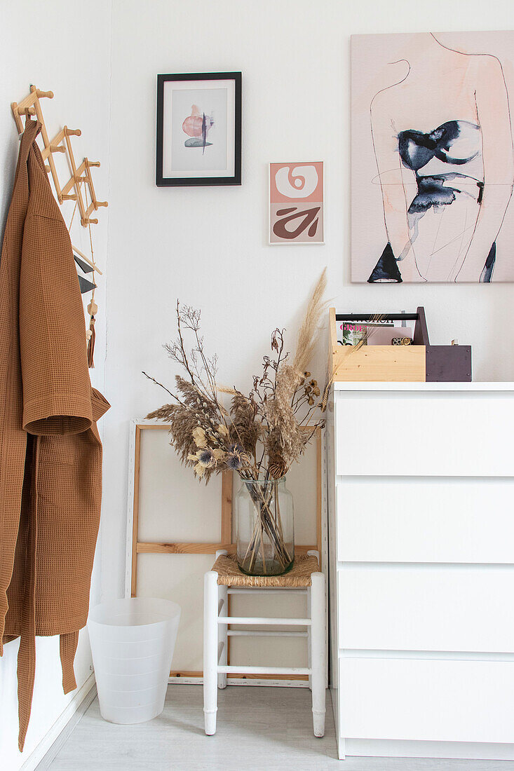 Corner with white chest of drawers, dried flowers and pictures