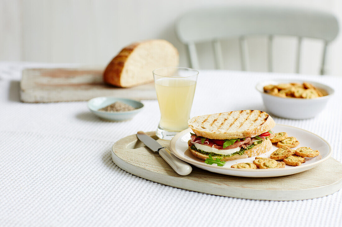 Sauerteig-Sandwich mit Schinken, Mozzarella und Salat, dazu Cracker und Apfelsaft