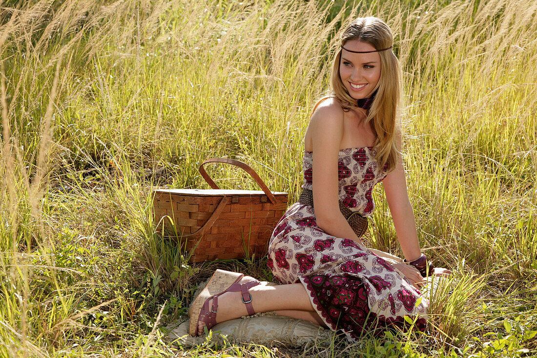 Blonde Frau im schulterfreiem Sommerkleid mit Picknickkorb auf der Wiese