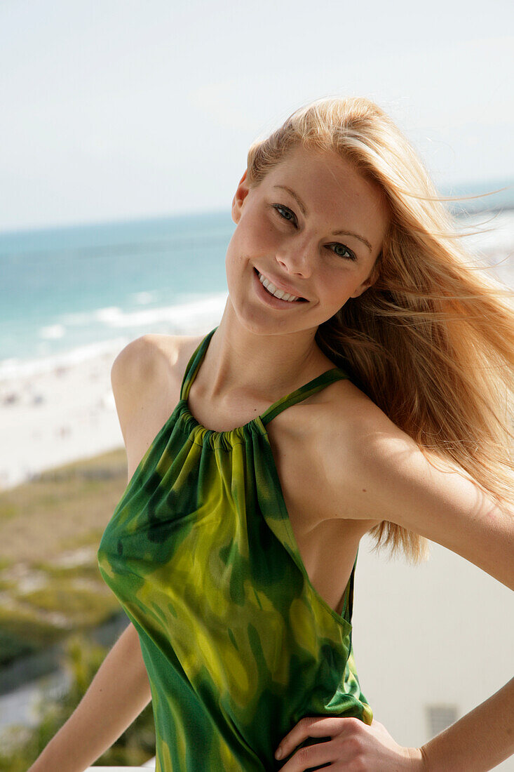 Blonde Frau in grünem Neckholder-Kleid am Meer