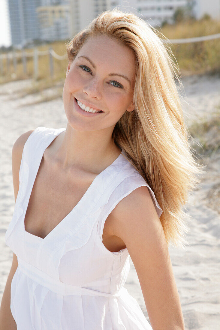 Blonde woman in white summer dress on the beach