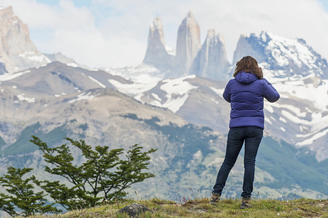 Eine Frau steht mit Blick auf die zerklüftete Berglandschaft, Torres Del Paine Nationalpark; Torres Del Paine, Magallanes und Antartica Chilena Region, Chile