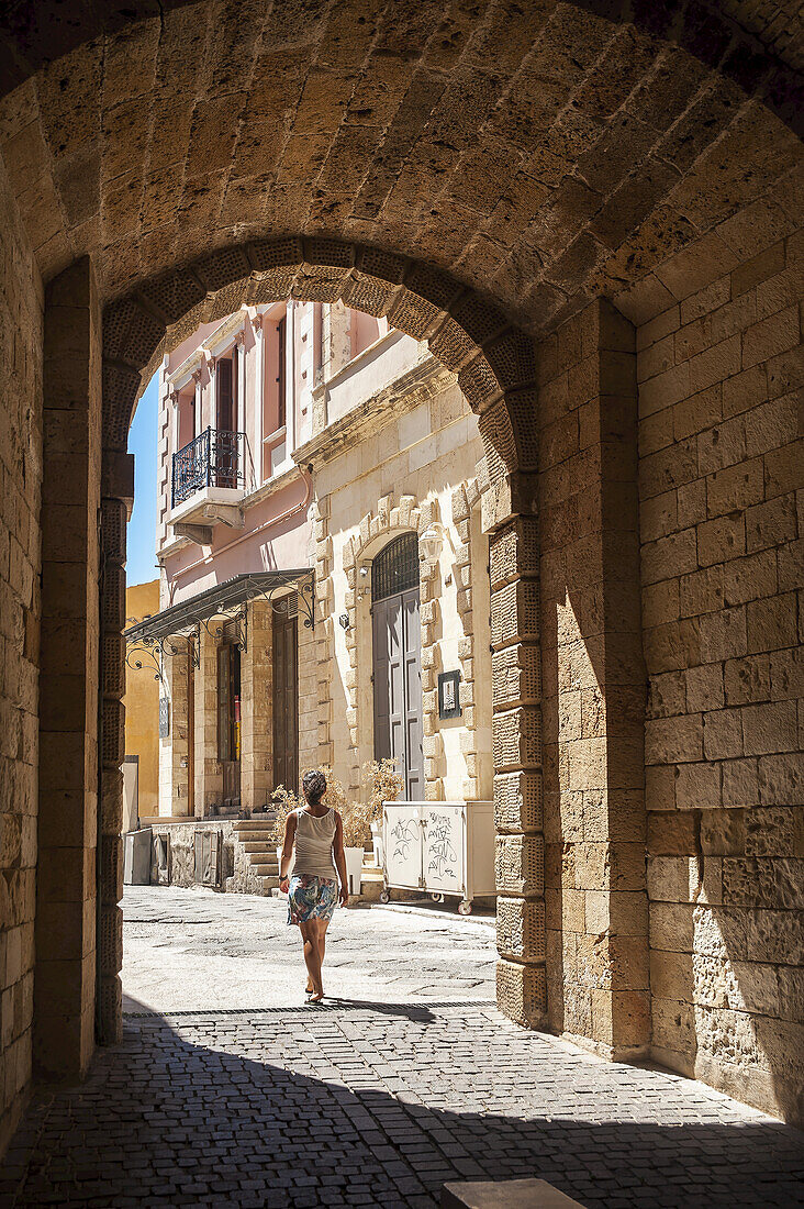 A Woman Walks Through An Arched Walkway; Chania, Crete, Greece