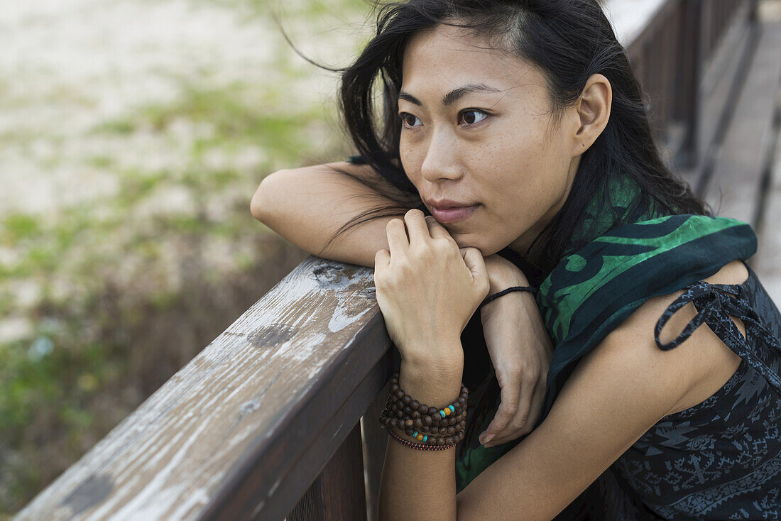 A Young Woman Sits Against A Wooden Railing Looking Out At The Ocean; Jincheng, Kinmen, Taiwan