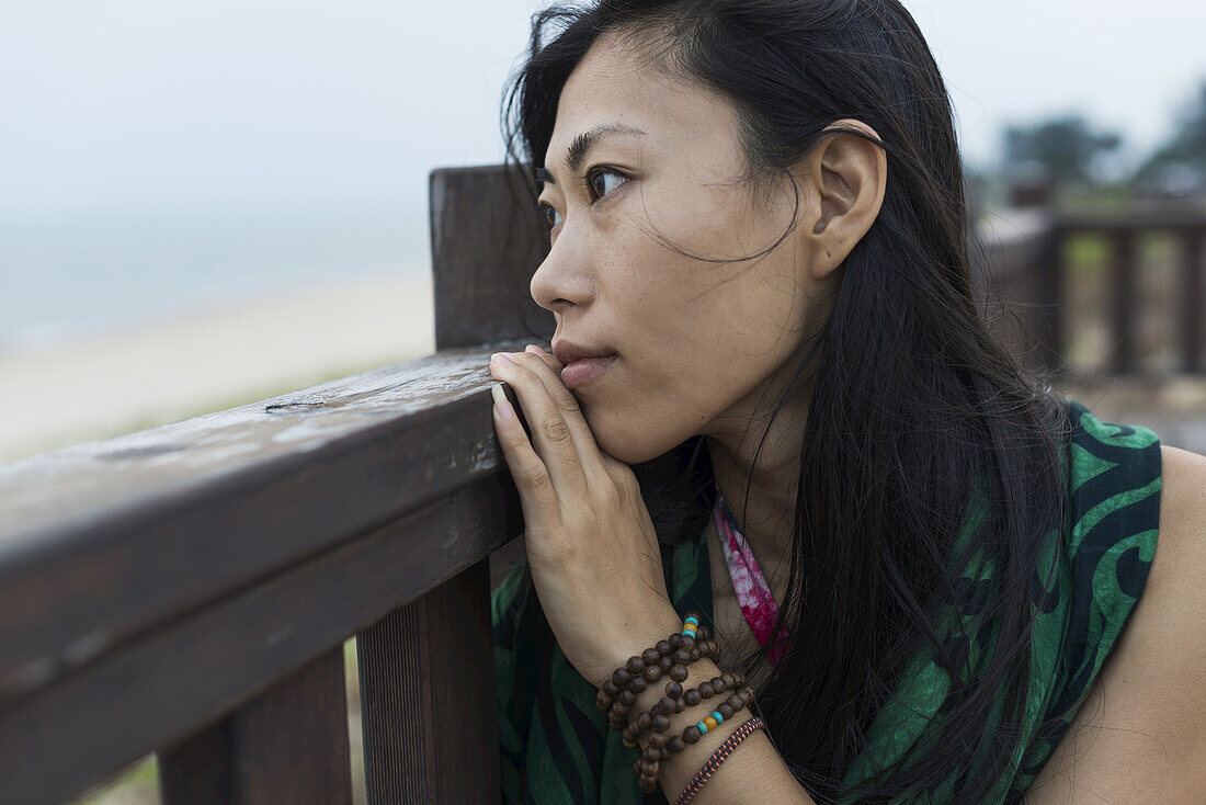 Eine junge Frau sitzt an einem Holzgeländer und blickt auf den Ozean; Jincheng, Kinmen, Taiwan