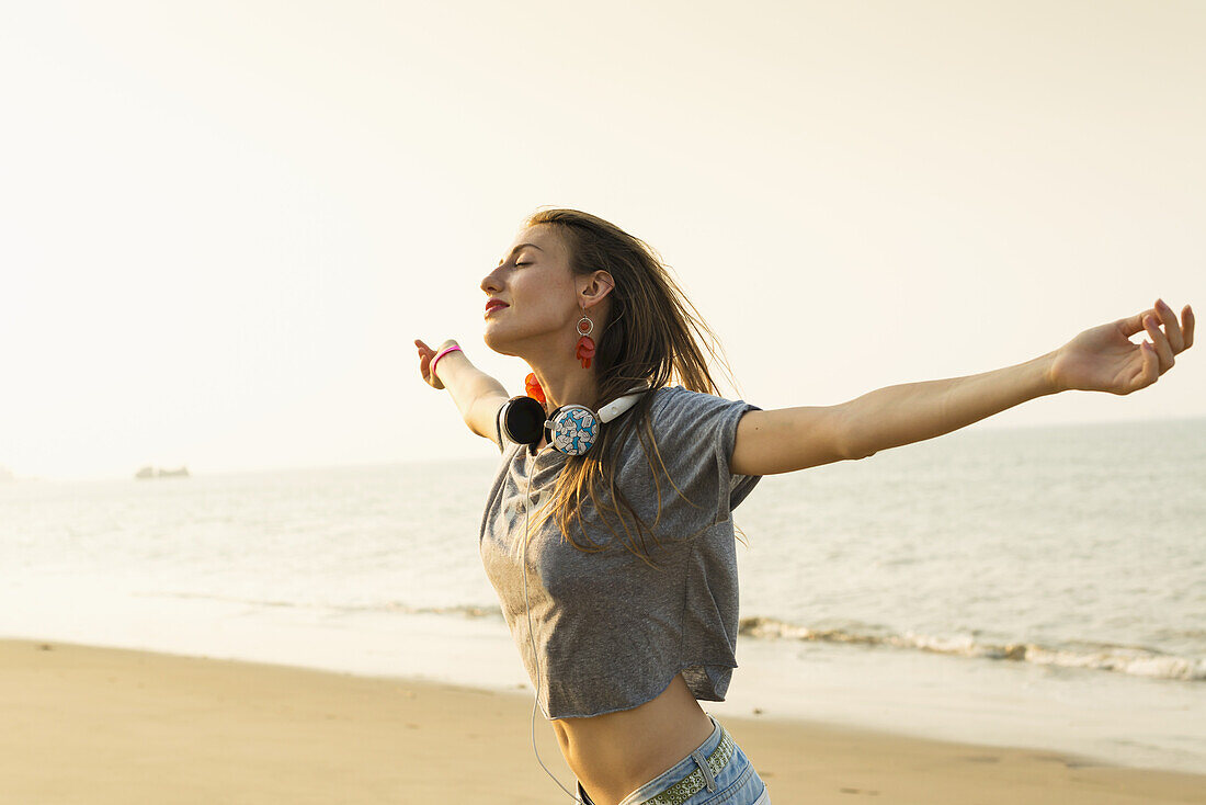 Junge Frau, die mit ihren Kopfhörern am Strand Musik hört; Xiamen, China