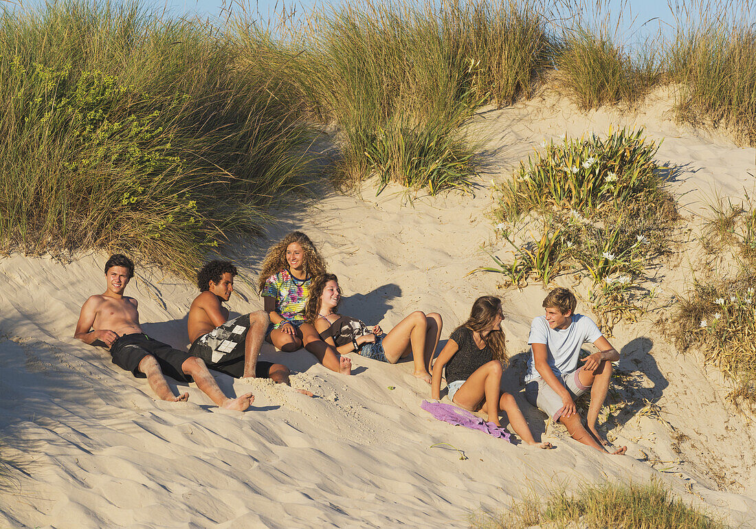 Eine Gruppe von Teenagern, die im Sand liegen; Tarifa, Cadiz, Andalusien, Spanien