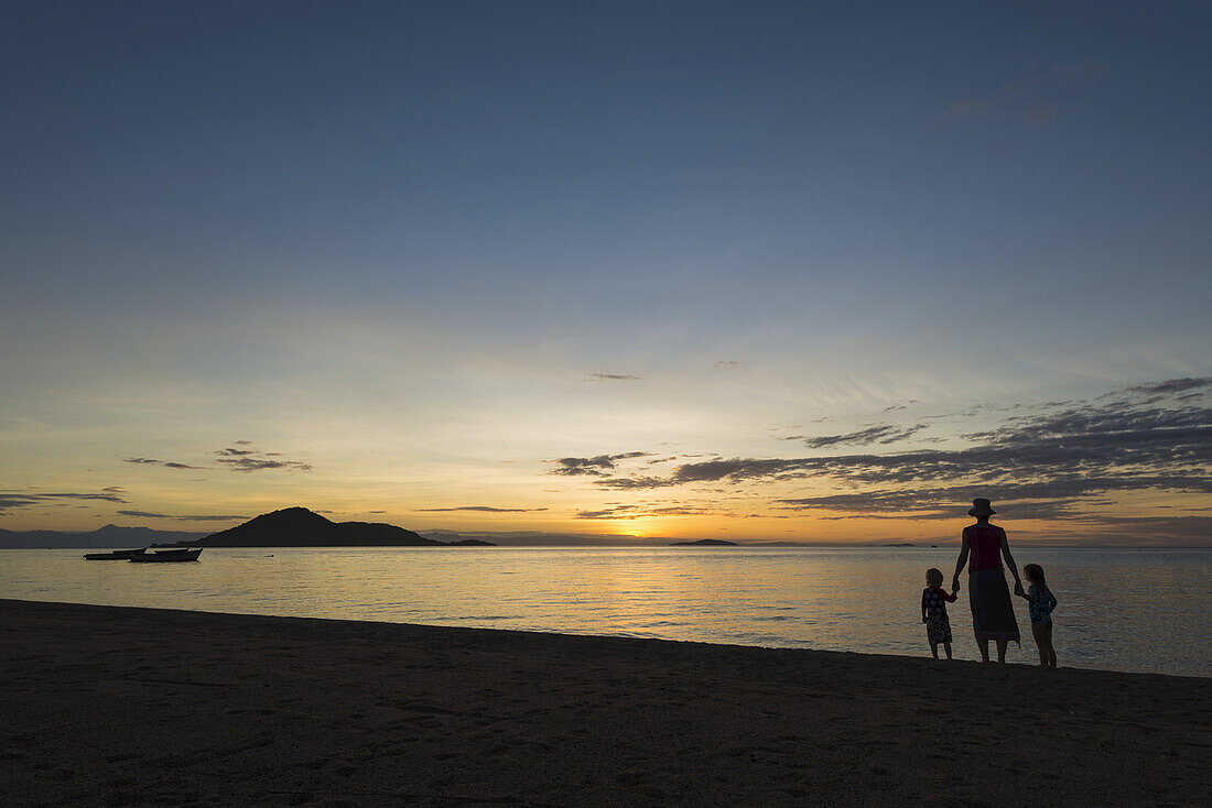Silhouette einer Mutter mit Junge und Mädchen am Strand von Cape Maclear bei Sonnenuntergang, Malawisee; Malawi