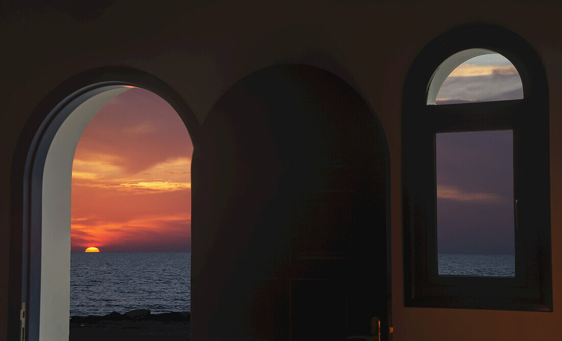 Blick auf einen farbenfrohen, dramatischen Sonnenuntergang über dem Meer durch einen Torbogen; Paphos, Zypern