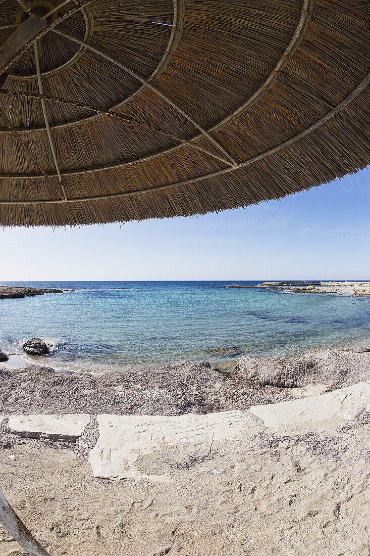 Blick auf das Mittelmeer unter einem strohgedeckten Regenschirm am Wasser; Paphos, Zypern