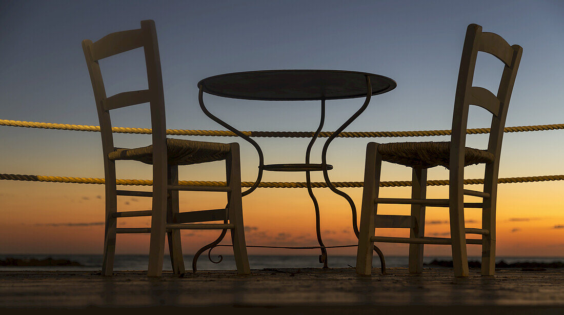 Ein Tisch und Stühle auf einer Terrasse mit Blick auf einen farbenfrohen Sonnenuntergang; Paphos, Zypern