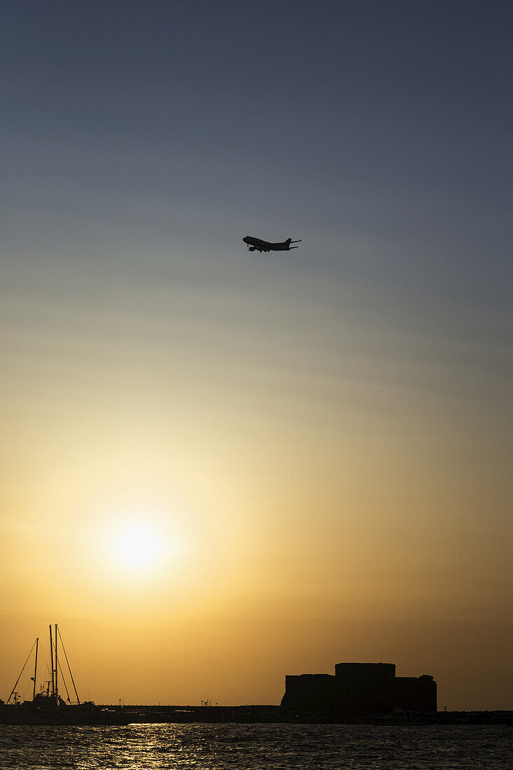Flugzeug fliegt über den Hafen bei Sonnenuntergang; Paphos, Zypern